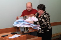 Представительница избирательной комиссии вынимает бюллетени из комплекса обработки избирательных бюллетеней (КОИБ)