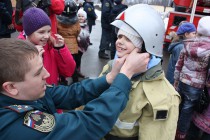 Специалист МЧС помогает школьнице снять экипировку пожарного