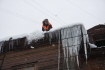Рабочий при помощи лопаты сбивает сосульки с крыши